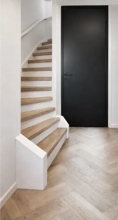 Gerenoveerde trap met lichte houtlook treden en witte stootborden naast een zwarte deur