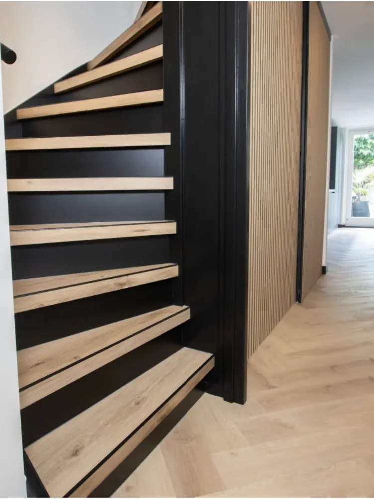 Trap met lichte houtlook treden en zwarte stootborden naast een lattenwand