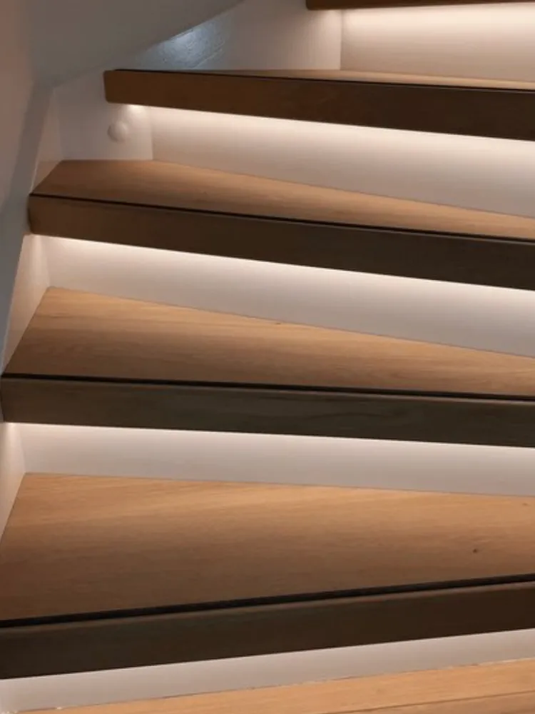 Trap met donkere houtlook treden en verlichting langs de wand